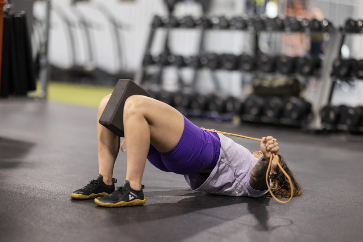 Coach Jacqueline demonstrating a glute bridge exercise with a band across her hips during a strength training session.