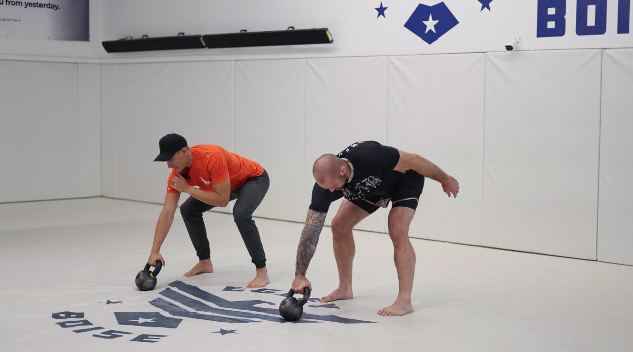 Athletes practicing kettlebell hinge movement on a jiu-jitsu mat to train selective tension and relaxation for improved conditioning and performance